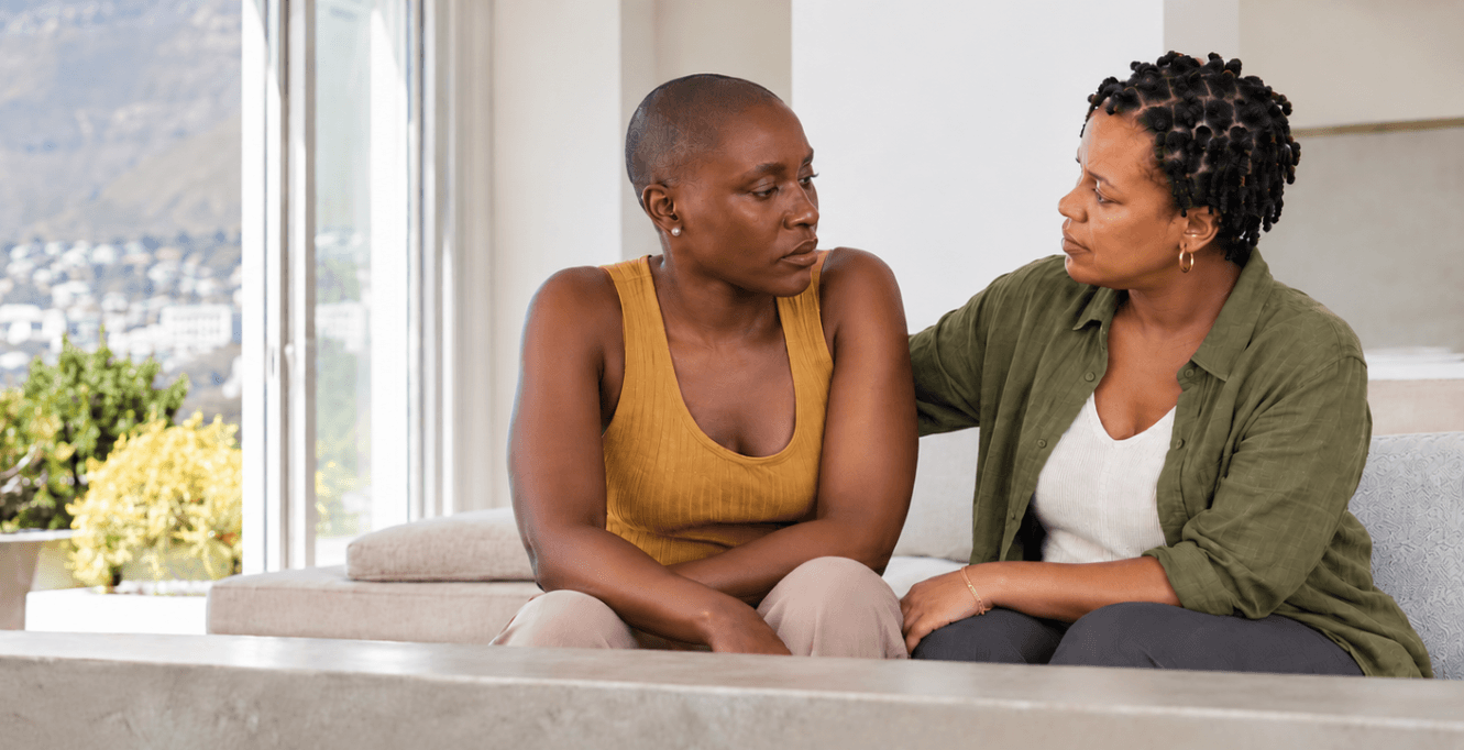 One woman rests a supportive hand on another’s shoulder as they sit together, reflecting the care needed when someone’s relationship with food or their body is difficult.