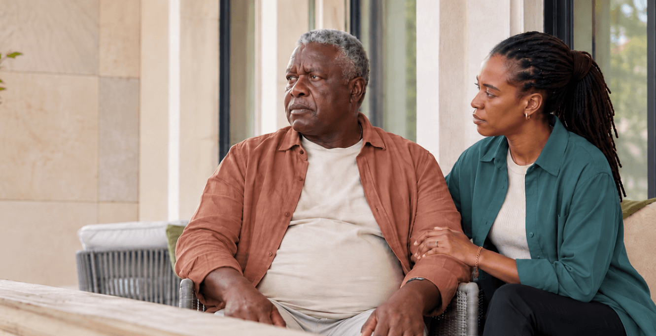A woman sits beside an older man and rests a hand on his arm, capturing the concern and closeness that can come with caregiving.